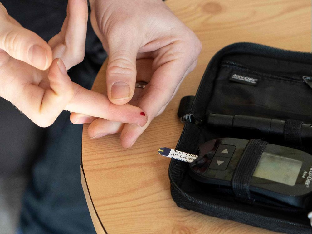A man with Type 1 diabetes prepares to place a drop of blood on a test strip inserted into a device to measure blood sugar levels. A better technology exists, but the RAMQ won't cover it, Michaella Etienne writes.