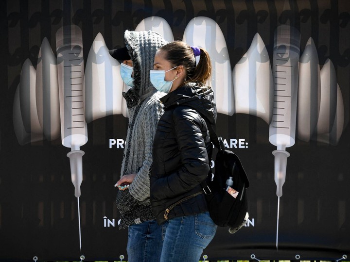  People wearing protection masks walk by a banner showing syringes as vampire fangs during the vaccination marathon organized at the “Bran Castle” in Bran village on May 8, 2021.