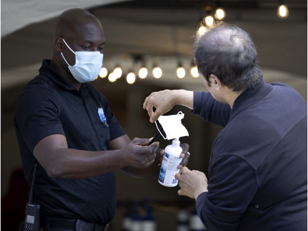 a security guard helps a man disinfect his hands and change masks before he enters the covid-19 vaccination centre at the bill durnan arena in montreal on wednesday, july 21, 2021.