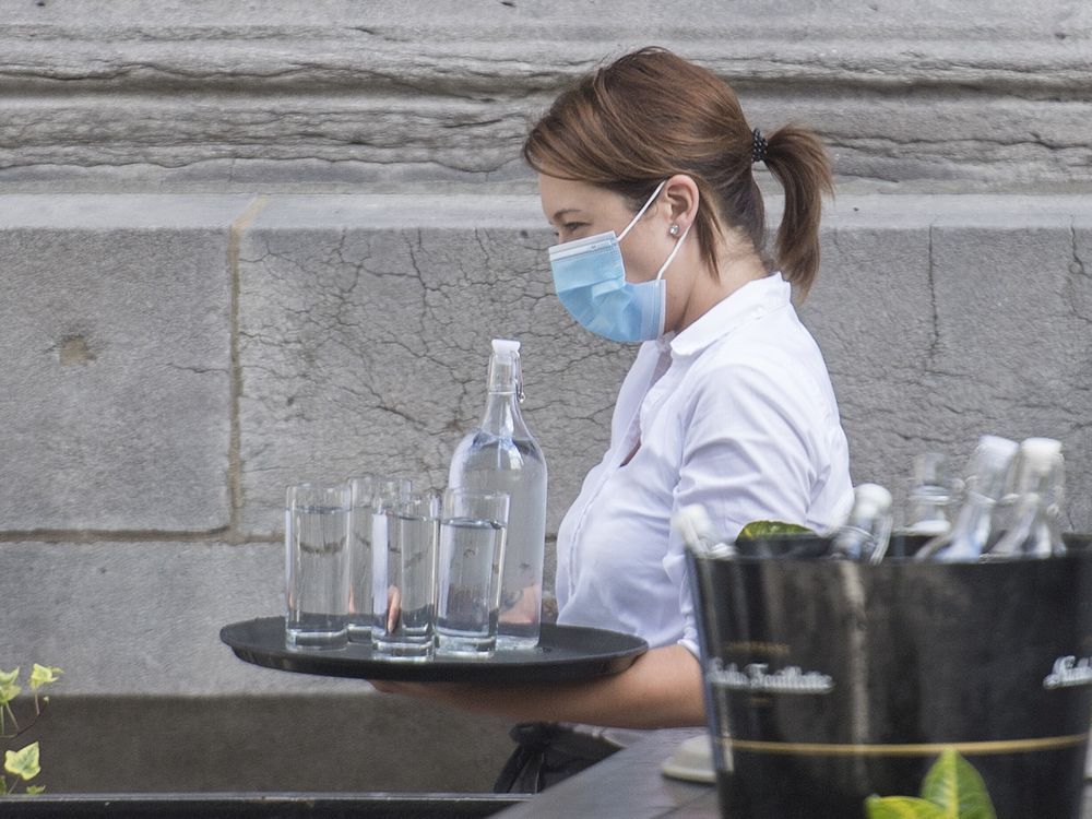 file: a server wears a face mask as she carries a tray of glasses and water at a restaurant.