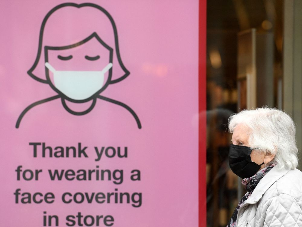 a member of the public wearing a face mask passes a sign reminding shoppers to wear face coverings inside a store.