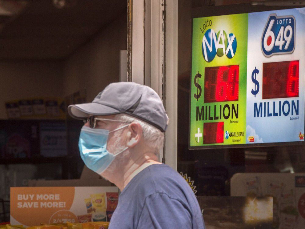 a pedestrian wearing a mask walks past a lottery sign 649 sign on toronto's danforth avenue