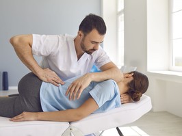 Man doctor chiropractor or osteopath fixing lying womans back in manual therapy clinic