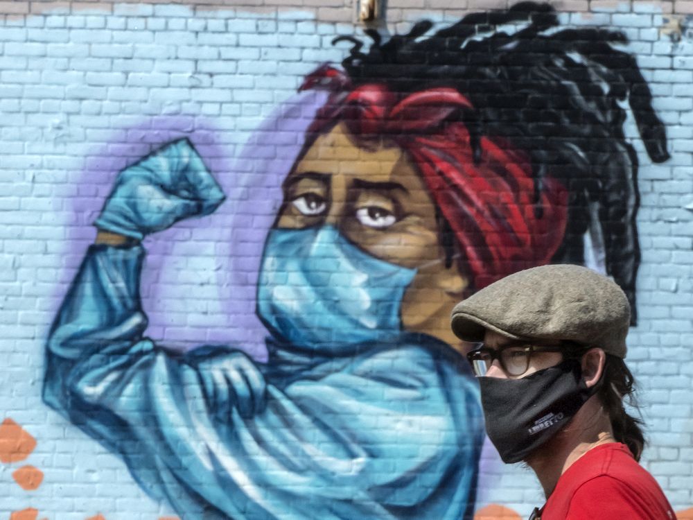 files: a pedestrian wearing a mask walks past a mural of a woman flexing her muscles while wearing a mask on toronto's dundas street during the covid 19 pandemic, friday august 28, 2020