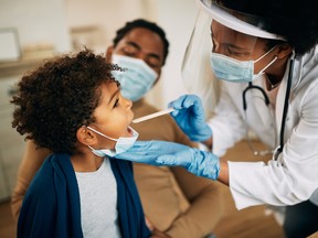 African American doctor with face mask examining boy's throat during a home visit.