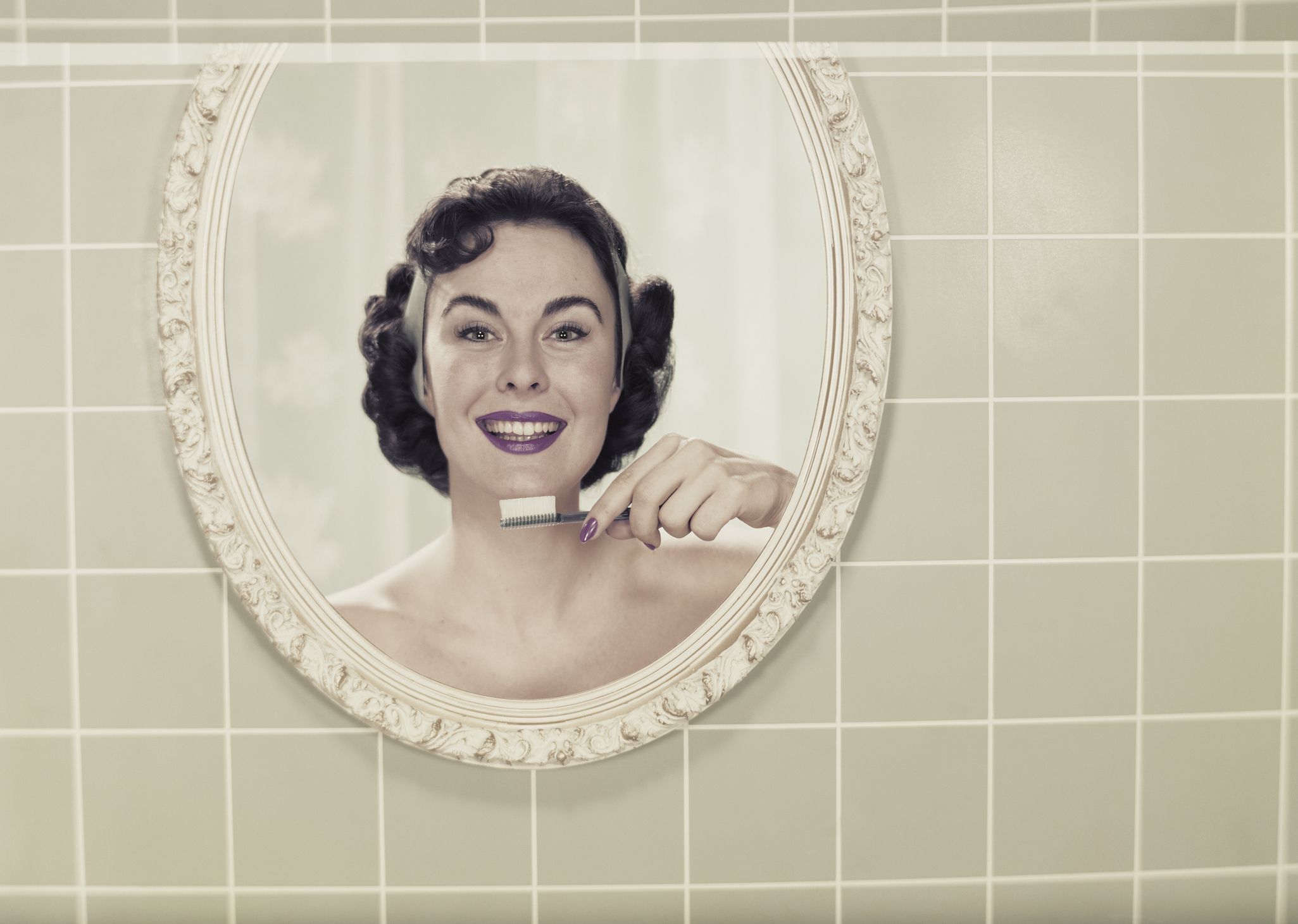 Young woman's reflection in mirror holding toothbrush, smiling, portrait