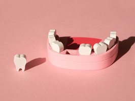 Wooden model toy of a human jaw with a missing tooth on pink background