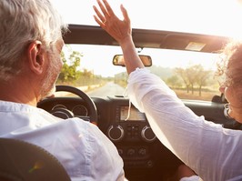 Mature Couple Driving Along Country Road In Open Top Car