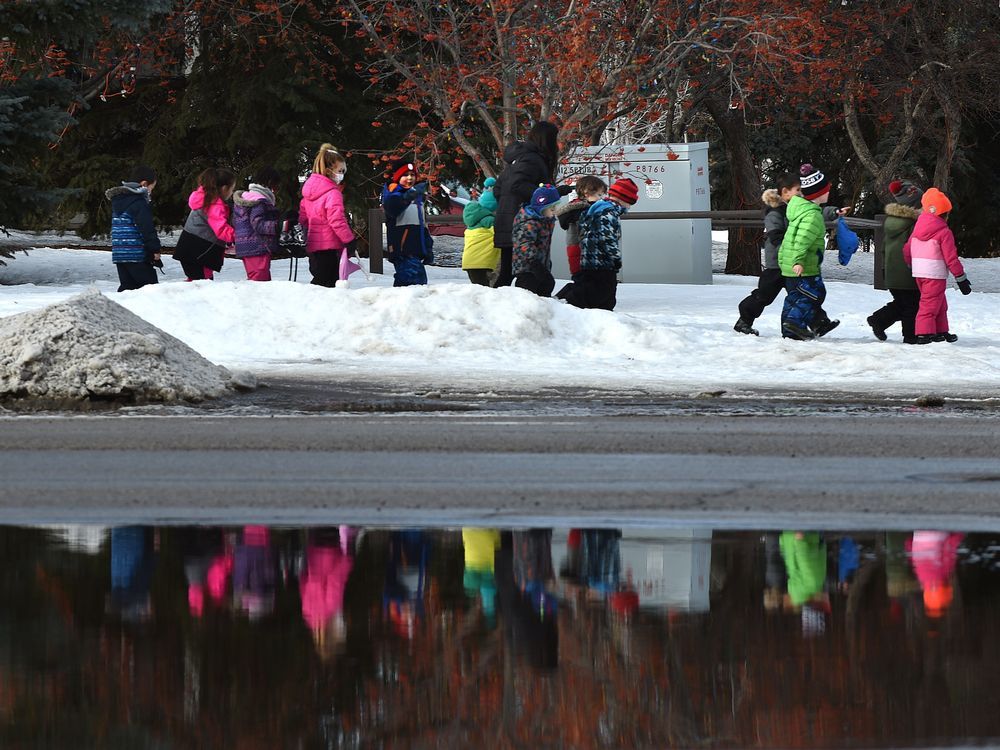 A group of children are reflected in a large puddle of water on the roadway while walking along the sidewalk on Riverbend Rd. as warm weather still persists in Edmonton, February 9, 2022.