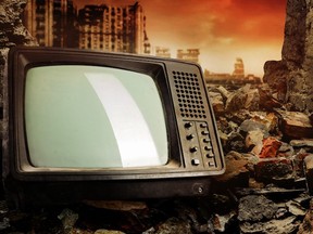 Old fashioned tv set laying on pile of bricks on ruined city wasteland.