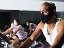 Man in protective mask ride stationary bike in a fitness club