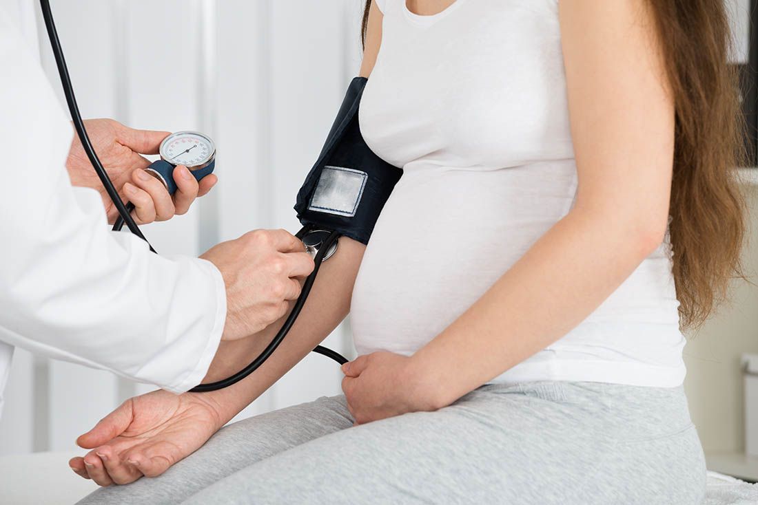 Close-up Of Male Doctor Measuring Blood Pressure Of Pregnant Woman In Clinic
