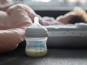 Close up selective focus on breast or formula milk in the baby bottle on the bed at home with sleeping baby infant in background - newborn feeding and nursing concept concept copy space