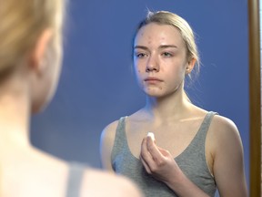Young lady with face puberty pimples looking in mirror and holding cotton pad