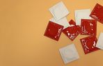 Mehrere ungeöffnete rote und weiße Kondome auf orangefarbenem Hintergrund, Konzept der sexuellen Prophylaxe