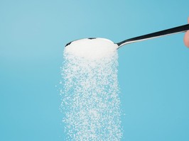 Hand pouring sugar from spoon isolated on blue background