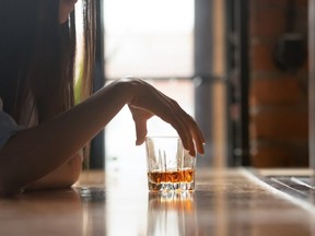 Sad young drinker holding whiskey glass drinking alone in bar