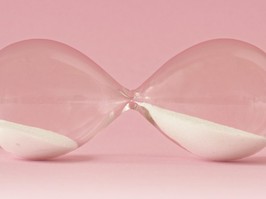 Hourglass lying on pink background - Concept of time and woman
