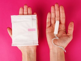 Woman holding menstrual tampon on a pink background. Menstruation time. Hygiene and protection