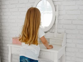 The girl looks in the mirror. Behind the ladies' table. Dressing table.