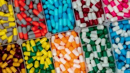 colorful capsule pills in plastic box. pharmaceutical industry. pink, yellow, blue, green, orange, gray, red, and white capsule pills. healthcare and medicine. vitamins and supplements concept.