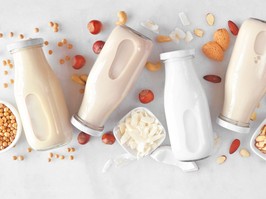 Vegan, plant based, non dairy milk milk bottles with scattered ingredients over white marble