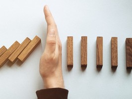 Wide view image of male hand stopping falling dominos. Over blue background.