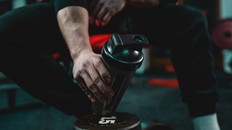 Close up on hand of unknown caucasian man holding dark supplement shaker while sitting at gym during training copy space selective focus