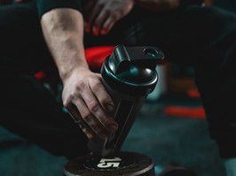 Close up on hand of unknown caucasian man holding dark supplement shaker while sitting at gym during training copy space selective focus