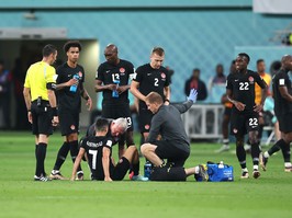 Stephen Eustaquio of Canada sits on the WOrld Cup pitch during a game against Croatia; he is tended to by a medical professional