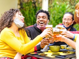 Happy group of multiracial friends with face mask drinking and toasting beer at brewery bar restaurant - New normal lifestyle concept about friendship with young people having fun together in pub