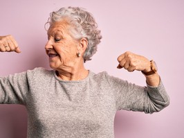 Senior beautiful woman wearing casual t-shirt standing over isolated pink background showing arms muscles smiling proud. Fitness concept.