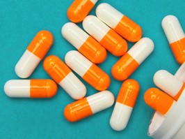 Orange white capsules (pills) were poured from a white bottle on a blue background. Medical background, template.Orange white capsules (pills) were poured from a white bottle on a blue background. Medical background, template.