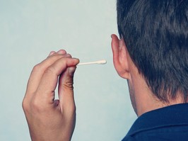 man cleans his ear with a cotton swab close-up on blue background