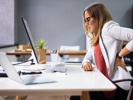 Woman sitting at her desk experiencing lower back pain.