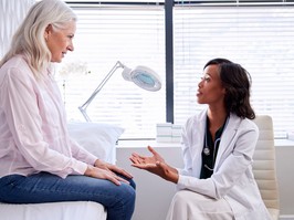 Mature Woman In Consultation With Female Doctor Sitting On Examination Couch In Office
