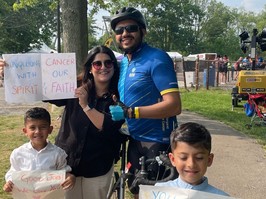 A family of four — mother, father, and two children — stand holding signs celebrating how they raised money for immunotherapy for glioblastoa, an agressive form of brain tumour