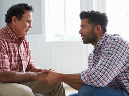 Older man and younger man holding hands in a bedroom. Younger man is comforting the older man.