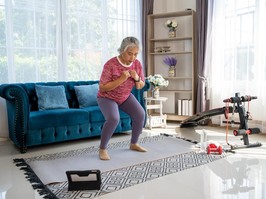 Woman exercises in her living room surrounded by workout equipment.