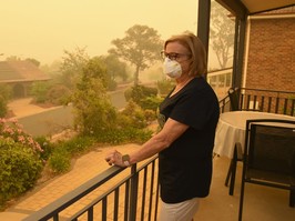 Woman wearing a mask standing on a balcony surrounded by a haze of smoke.