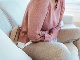 Cropped shot of a young woman holding her stomach in pain on a couch.