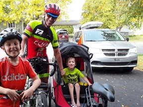 Bernard McNeil, Noah and Malik Trépanier. Grandfather stands with grandsons wearing cycling gear.