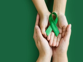Adult and child hands holds green ribbon on green background. World lymphoma awareness day. September 15. Liver, Gallbladders bile duct, kidney Cancer and Lymphoma Awareness month. Banner. copy space