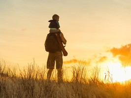 Father carrying son on his shoulders looking off into the sunset.