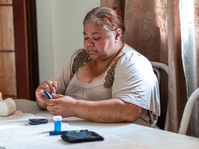 Portrait of a Latin woman at home checking her blood sugar levels, using a small pen to collect blood from her finger.