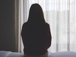 Rear view image of a woman sitting alone on a bed in bedroom.