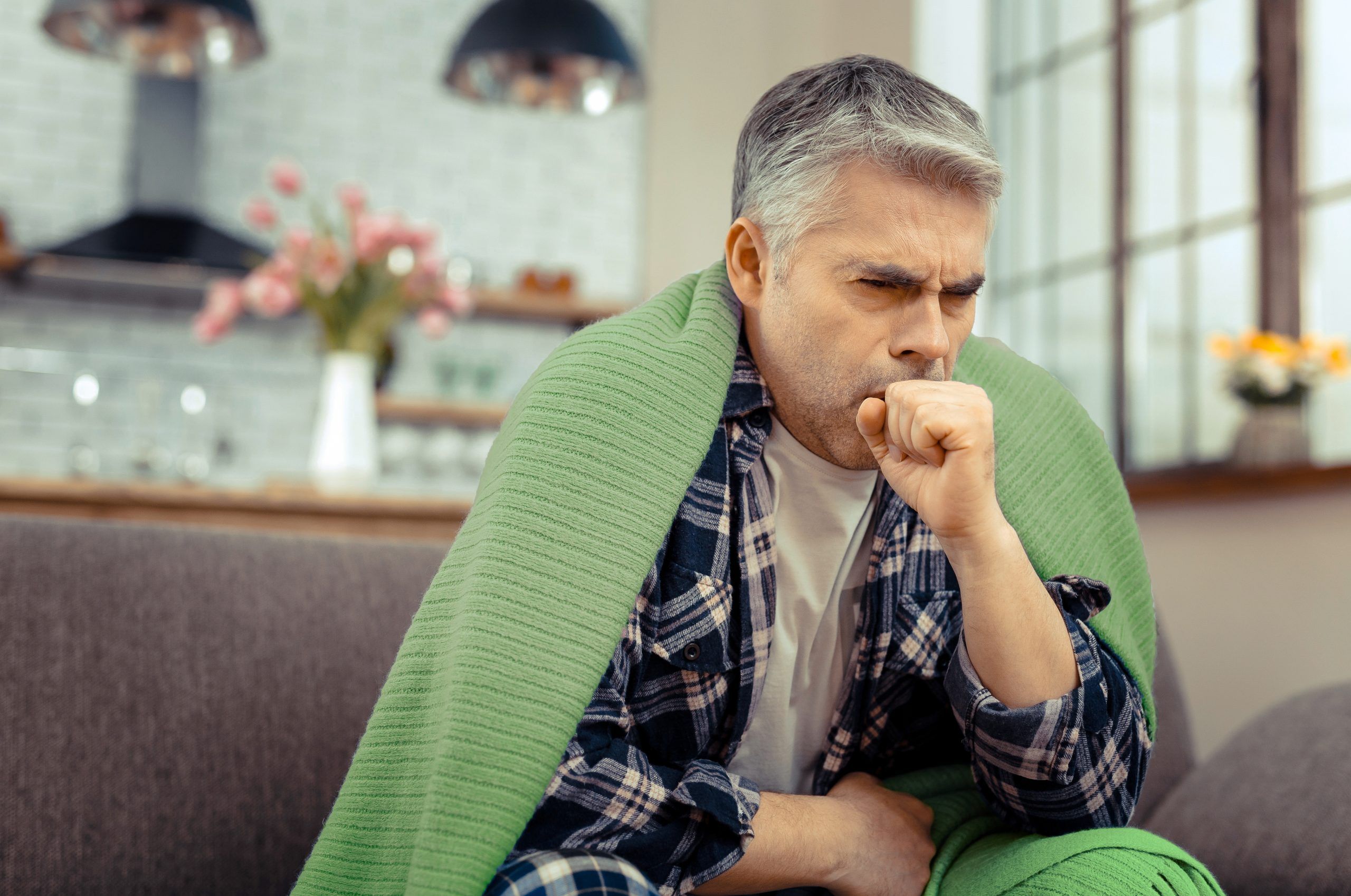 Suffering from cold. Unhappy cheerless man coughing into his hand while suffering from cold