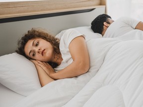 Woman and man laying back to back in bed. Woman looks upset.