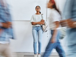 Young woman standing against a wall as crrowd walks by in a blur.