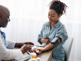 Gestational Hypertension. Mature Male Medical Worker Measuring Arterial Blood Pressure Of Pregnant Black Woman Using Cuff, Patient Having Problems With Tension, Sitting At Table. Health Care Concept